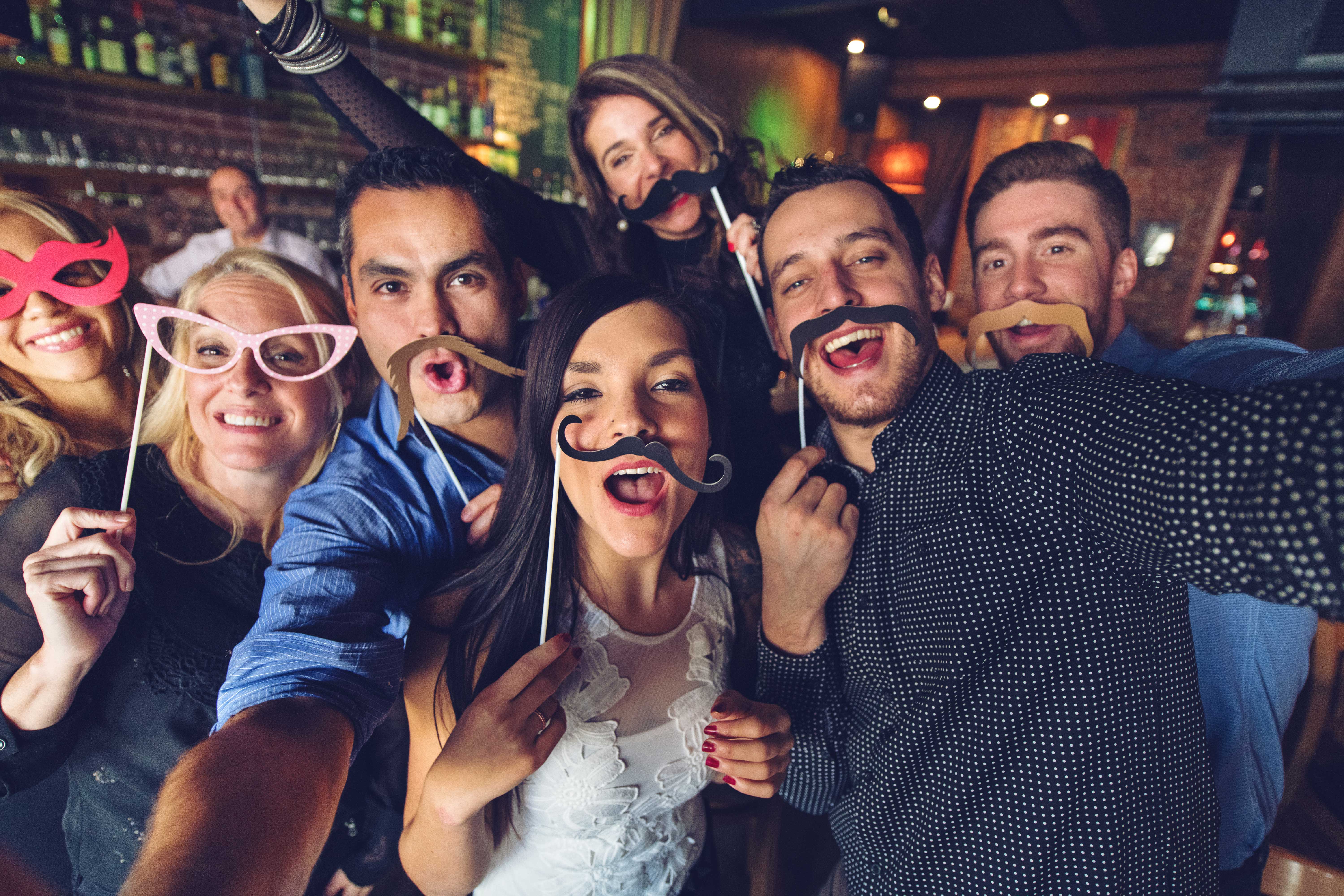 Group posing at an open air photo booth with props in a bar