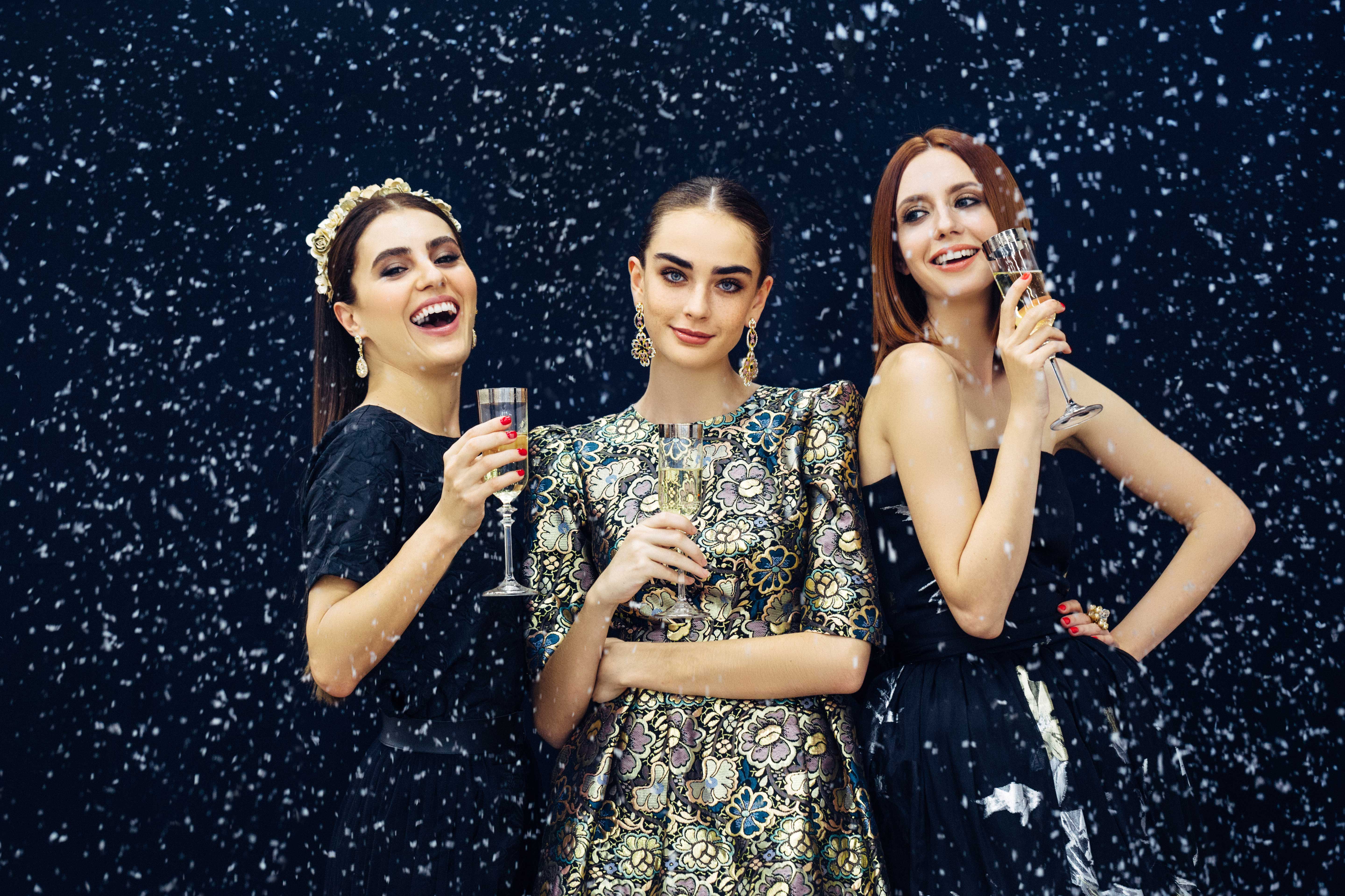 Three women posing for a photo booth photo at a New Year's Eve event with fake now falling